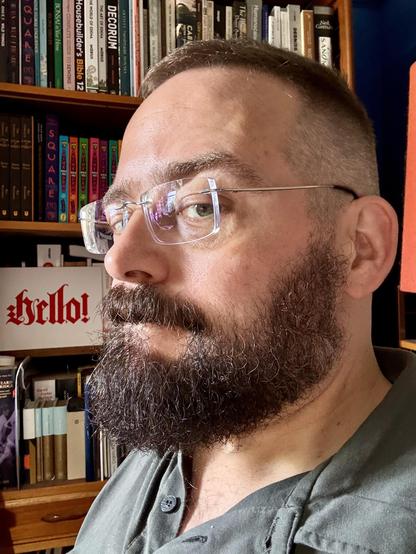 Me giving kinda-side-eye to the camera to show the fresh fade on my haircut. Behind me is a bookshelf with a hand-painted sign saying “hello!”