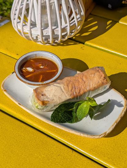 Summer roll sitting in the plate with mint leaf and peanut sauce