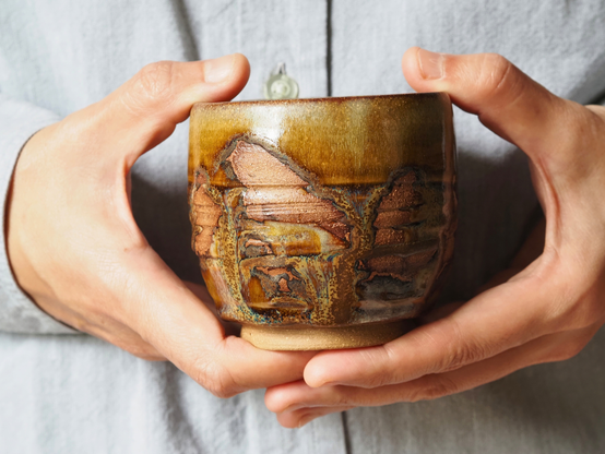 Handmade Japanese tea cup (yunomi) in warm autumnal colors with hand-carved lines. The yellow-gold glaze flows and pools in blue and gold flecks. In several parts, the glaze has been wiped off to show reddish ochre stoneware body.