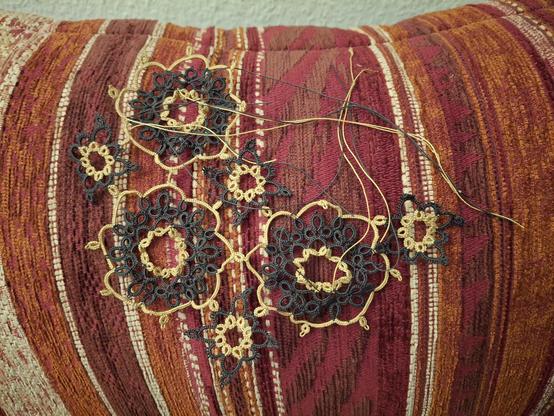 On sofa pillow lies a half finished lace doily, which has about a dozen loose end hanging from it.