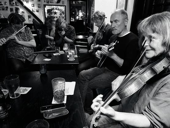 A pub table surrounded by musicians: flute, harmonica, mandolin, and fiddles.