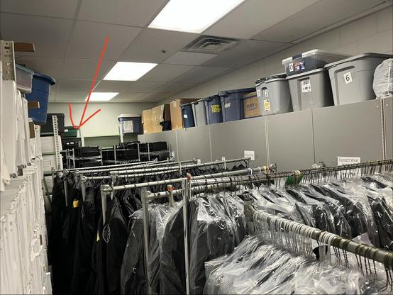 Photo of band closet, full of marching band uniforms, concert wear, music, shakos and marching shoes. Location of spare shako wraps indicated by arrow, waaaaaay in the back.