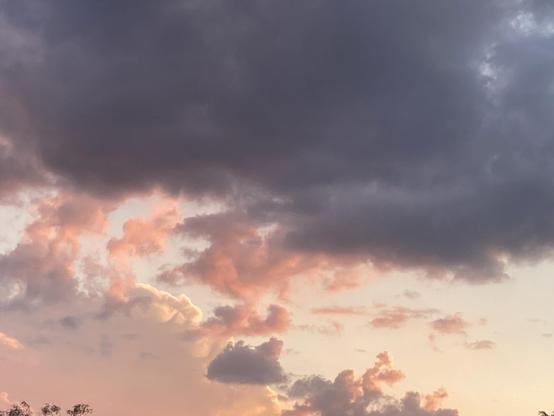 White, pink, and purple clouds are against a pale blue sky that tints to a warm yellow closer to the horizon.