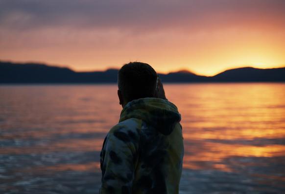 A man silhouetted while taking a photo of the sunset over water.
