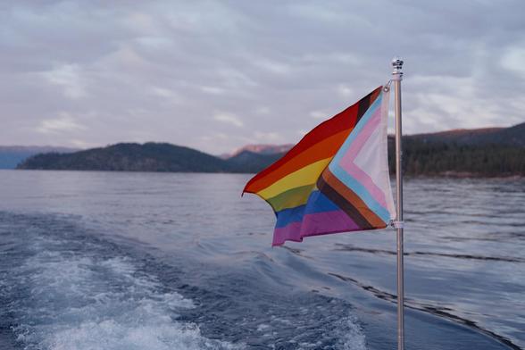 Progress pride flag extended in the air behind a moving boat.