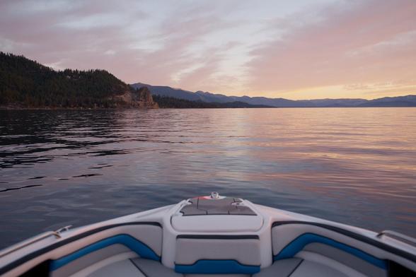 Looking off the front of a boat towards Cave Rock, a volcanic cone on the east shore of Lake Tahoe. Clouds are reflected over calm water.