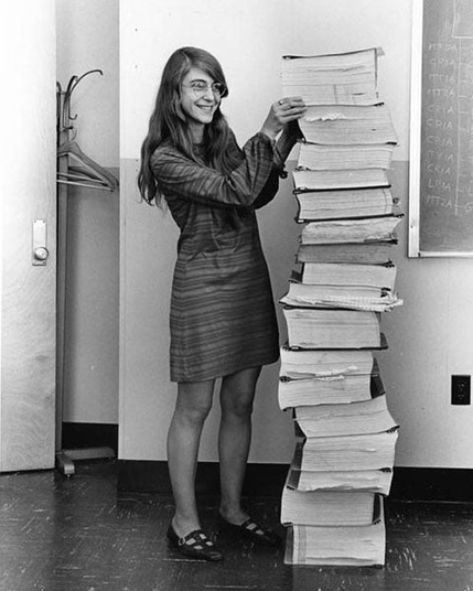 A B&W photo of a person standing next to a stack of printed paper as high as the top of their head. This is Margaret Hamilton, at work as a Software Engineer and the leader of a team of extremely specialised programmers who worked for NASA. The photo was taken in 1969, and it shows a physical form if her work since she joined the Apollo project in 1965 (she joined at the age of 29 by my calculation). My interpretation of the expression on her face is a mix of pride and mild amusement.  She has glasses, long, straight hair, and neat office attire. Margaret Hamilton has her hands placed gently on the stack of printouts to keep it all balanced upright. The pages appear to be arranged in bundles, ranging from 8-10 centimetres thick, to 20cm thick or more. The resulting stack of printouts is physically impressive for being an unusual feat, and it represents something even more impressive: it's the printed form of the source-code she and the team she led wrote for the NASA Apollo project. Their software ran on the Apollo Guidance Computer that was that on board each Apollo command module and Apollo Lunar Module. The Apollo Guidance Computer onboard the Eagle was an essential flight instrument for Neil Armstrong when he piloted the craft to land on the surface of the moon.