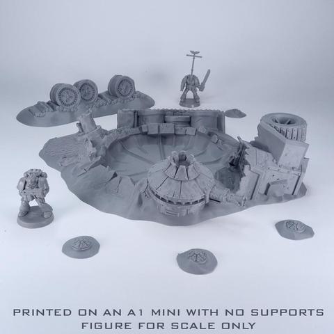 An unpainted grey crater with ruined vehicle parts around it, some mines and a couple of figures