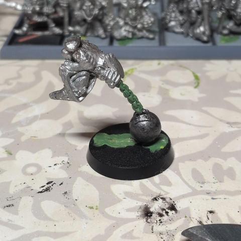 A picture of a metal goblin holding onto a green chain that is attached to a metal ball.