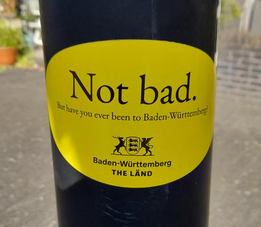 A lamp post with a yellow sticker saying Not bad. But have you ever been to Baden Württemberg? In English instead of the more usual German.