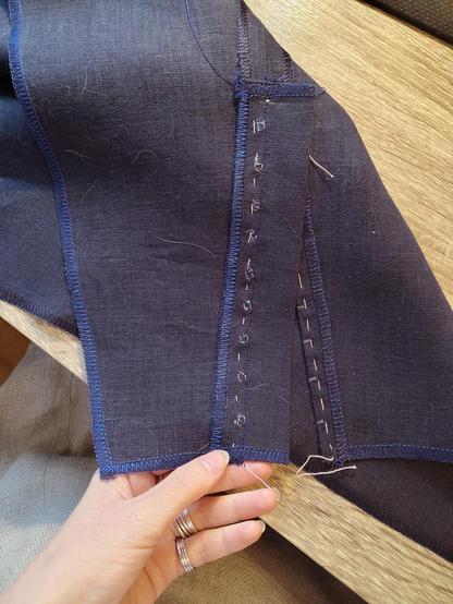 From the wrong side, showing the placket with its 1.5cm seam allowance going along with the seam allowance of the skirt piece itself, and the line of stitching joining them going over the hand sewn portions and the handles of the eyes. A nicely pressed corresponding part without the placket bit shown under. Tidy and shiny overlocking goes around every piece in a pretty blue.