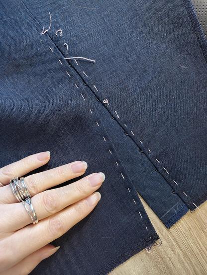 From the right side, showing how very flat and smooth and nice the placket is before topstitching! With judicious pressing on the turns and the ironed open seams, it looks quite lovely. There are two lines of tacking thread holding the turns perfectly in place. Only a little bit of the eyes peeks out, just the little loop where the hook goes, with no other sewing visible. There's a chalk marking of "UP" on the placket, to make sure it got sewn on the right way. Sini's very pale hand on the skirt fabric, also.