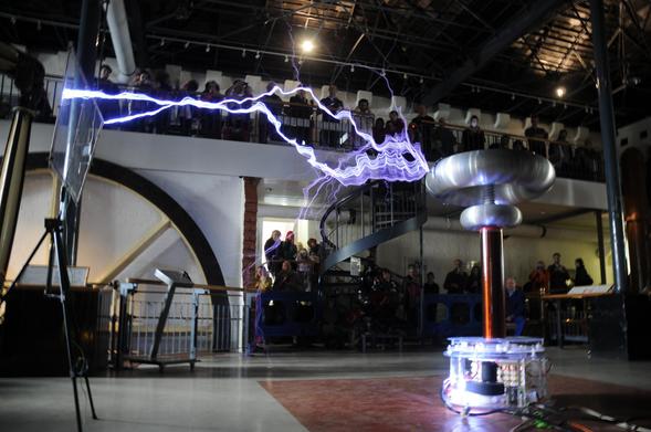 Picture from the Gaussfest. Tesla coil with a large electrical discharge in front of a crowd of people and a large flywheel