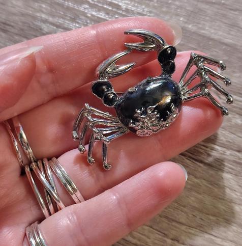 A very close up photo of a black and silver with glass crystal bits brooch in the shape of a jaunty crab. It's a little bit dusty on its enamelled black body, and one of its tiny little swarowski eyes is missing. It's quite cute if you like a crab.