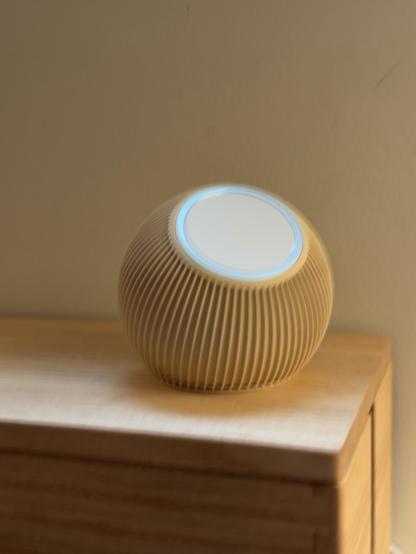 A round MagSafe stand with a textured surface is placed on a wooden surface. The background features a plain wall.