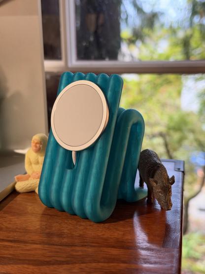 A vibrant turquoise MagSafe stand, accompanied by small figurines: a meditating sasquatch and a javelina.