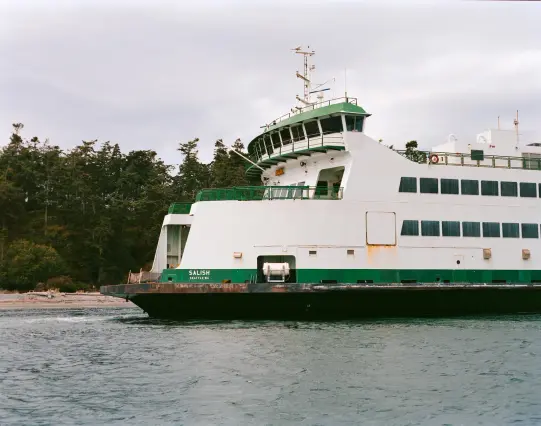 The ferry Salish Seattle WA approaching a rocky shoreline with evergreen trees.