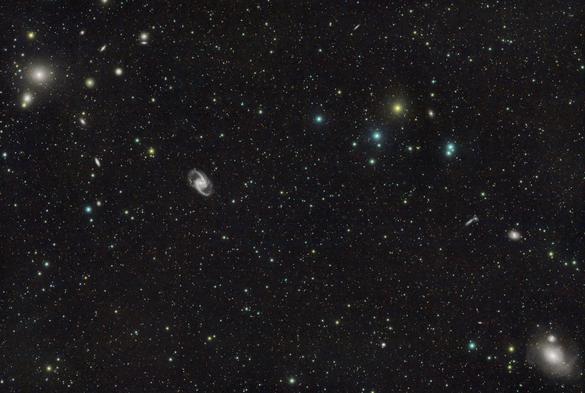 A collection of large and small galaxies on a foreground of stars. There is a dense group of fuzzy elliptical galaxies at top left and a very large one at bottom right.

Between those sits a very pretty barred spiral, looking a bit like a shuriken.

A bright orange star sits at top right.

Many smaller galaxies are dotted around, some elliptical, some spirals and some edge-on.