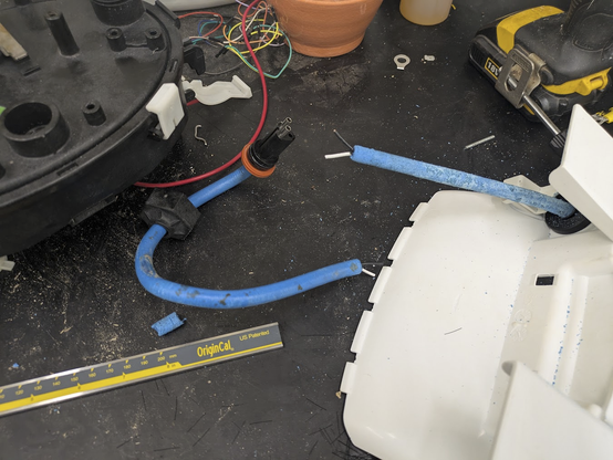 A photo of a workbench showing parts of a disassembled pool cleaning robot. In the centre is a blue cable with white and black cores inside. The cable has been chopped open to expose the cores.
