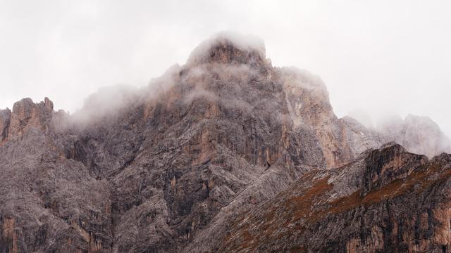 A rock face of a mountain with the top vanishing in the clouds.