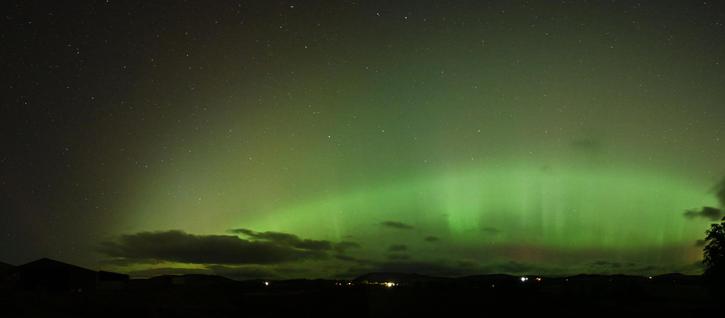A night dky Aurora panorama of a bright green arc of rays over a low dark horizon