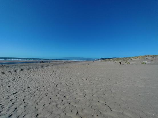 Looking north from Ocean Beach in San Francisco. Most of the scene is sand and blue sky, but to the west is the Pacific Ocean, with waves rolling in.