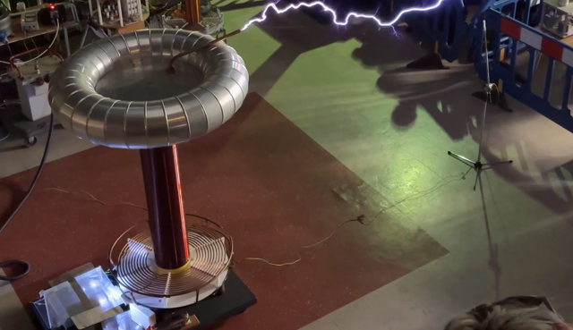 Looking down at a large Tesla coil. The rod on top of the coil is generating some very impressive sparks. Some forking through the air, some are hitting a rod placed in front of it. This one was *loud*.