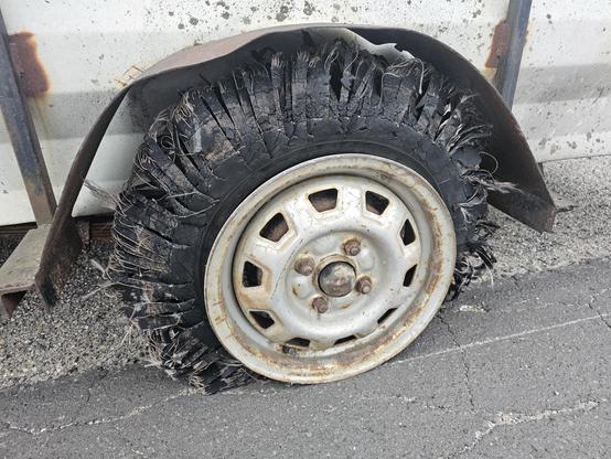 A trailer tire, badly blown out. The tread face has dissolved into little strips and loose radial belts. It looks kinda soft, actually, but it's not gonna be fixed.
