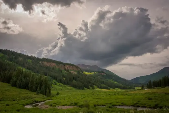 A winding stream flows through a lush green valley surrounded by forested mountains.
