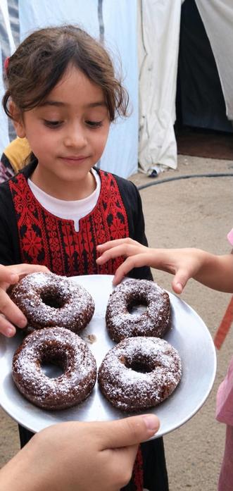 A little girl wearing traditional Palestinian dress enjoys a donut