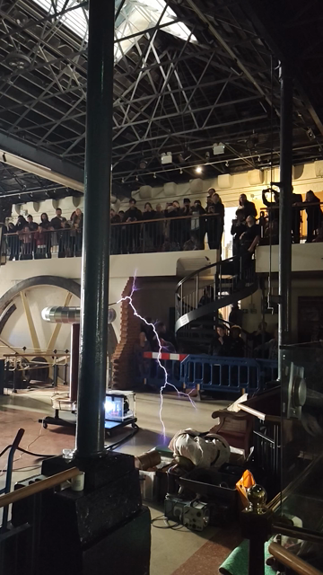 A unipolar coil tesla coil discharging into the air, the arcs of white-violet electricity reaching out as the coil-driven magnetic field ionises the air around it.