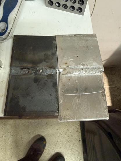 Two sets of two metal plates, the left ones relatively dirty steel, the right ones aluminum. The two steel plates are butt welded to each other, and the two aluminum plates also are.