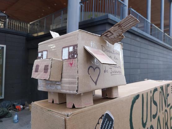 La tirelire de la cuisine solidaire de Jussieu, construite en carton pour former un cochon ailé sur (je crois) un modèle Minecraft (corps cubique, groin et pattes itou)