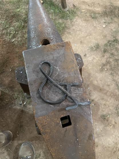 A serif ampersand forged from 1/4 steel laying on an anvil.