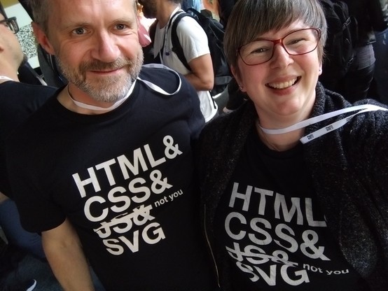 Paul and Sara in a selfie with matching T shirts, grinning.

T shirts say:
HTML&
CSS&
(strike out)JS&(end strikeout) not you
SVG