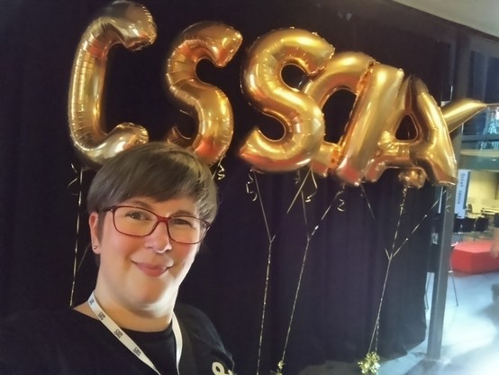 A chuffed Sara stood in front of big golden helium balloons spelling out CSSDAY.