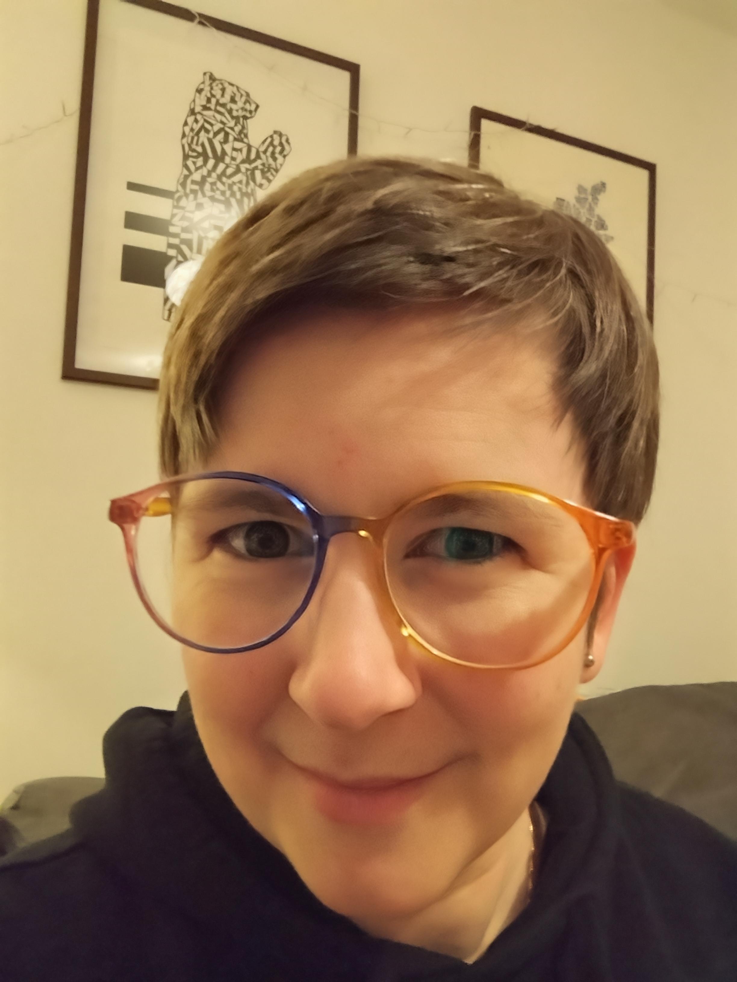 A selfie while wearing a pair of plastic glasses - oval/circular with a gradient of several colours across the frame.