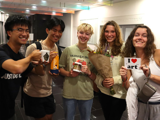 Five University of Georgia students pose for a photo at Student Night at the Georgia Museum of Art, two of them holding museum mugs that they won, one holding flowers, and one holding a postcard that says "I [heart] art"