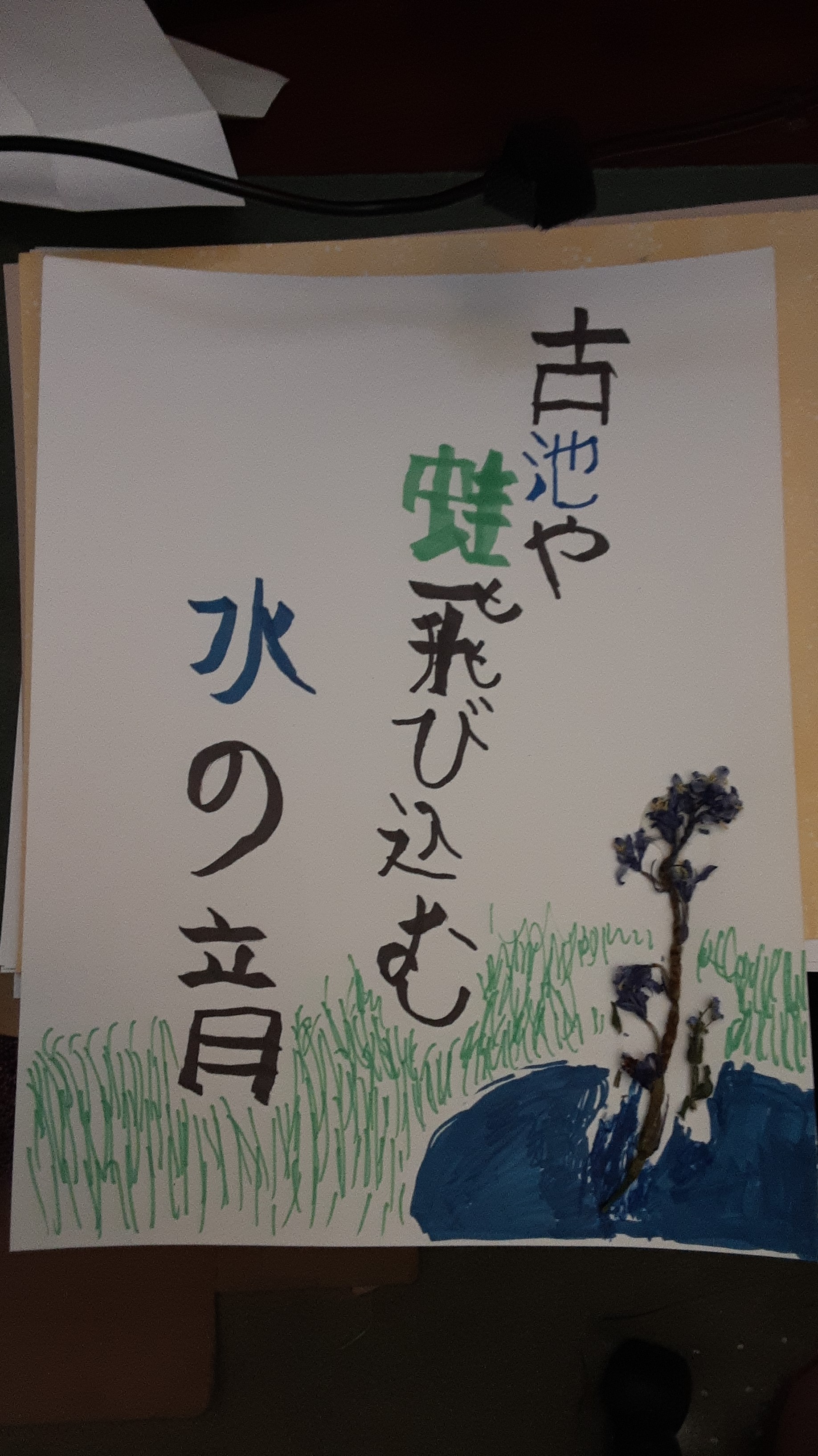 A rendering of Matsuo Bashō's poem: 

古池や　蛙飛び込む　水の音

Furu ike ya
kawazu tobikomu
mizu no oto

in mostly black marker over a drawing in marker of a pond and tall grass. There is a plant sticking out of the pond, plucked from my front yard and glued to the paper.

蛙 (kawazu) has been drawn in green, to represent the frog(s), and 池 (ike) and 水 (mizu) have been drawn in blue, to represent the pond and the water.