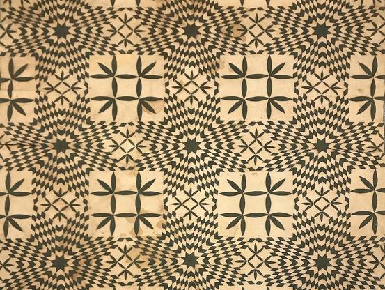 Detail of a 19th-century quilt made in Georgia, likely by an enslaved person. Instead of being brightly colored, it features black designs (stars, things that look like hashtags) on what is now an off-white backing. The patterns are intricate and beautiful.