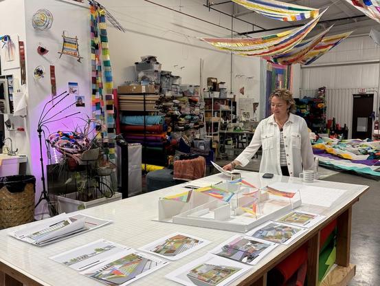 A color photograph of artist Rachel Hayes in her studio, working with a mockup of the Georgia Museum of Art's sculpture garden to plan her suspended textile sculptures there.