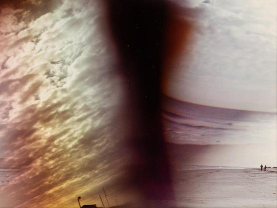 Detail of an abstract-looking color photograph by Judith McWillie. It seems to show a beach, the ocean, and the sky, but you can't exactly see them. There's a big dark vertical shape that goes all the way down the middle of the image that almost looks like a tornado.