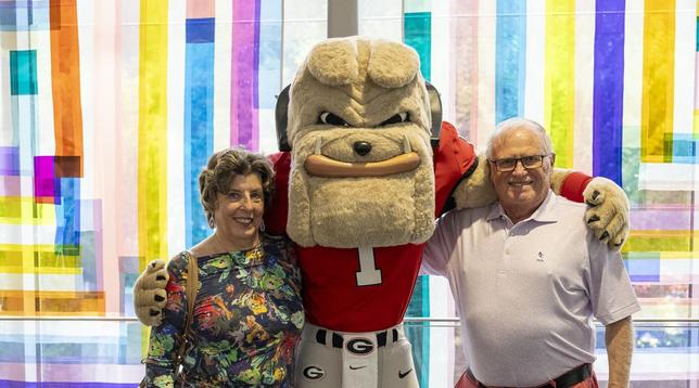 Jean Petrovs (left), a longtime community docent at the Georgia Museum of Art, poses for a photo with the University of Georgia mascot Hairy Dawg and her husband, Red Petrovs, at a museum event.