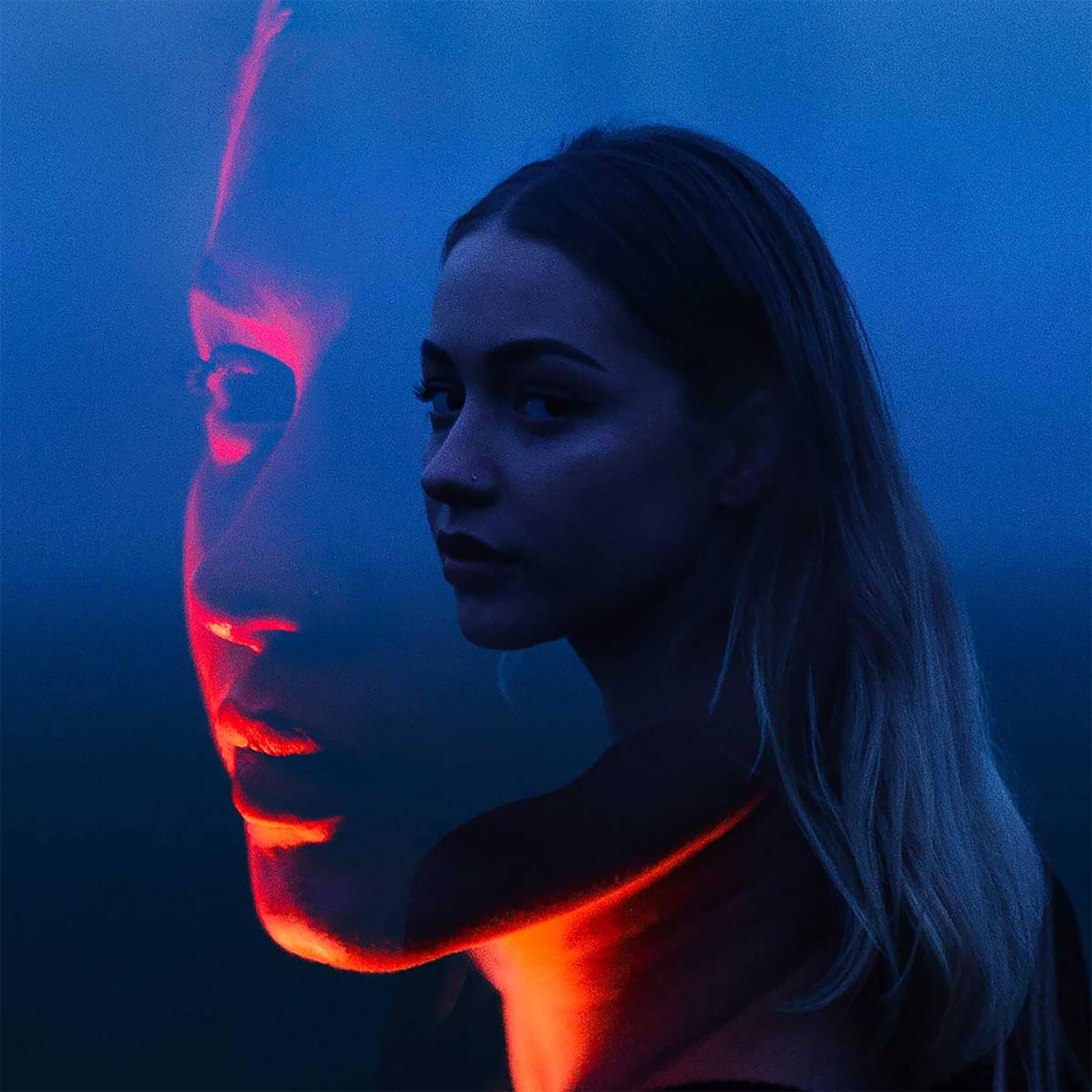 Cinematic double-exposure portrait of a woman against a deep blue background, with vivid red-orange light illuminating her face and neck.