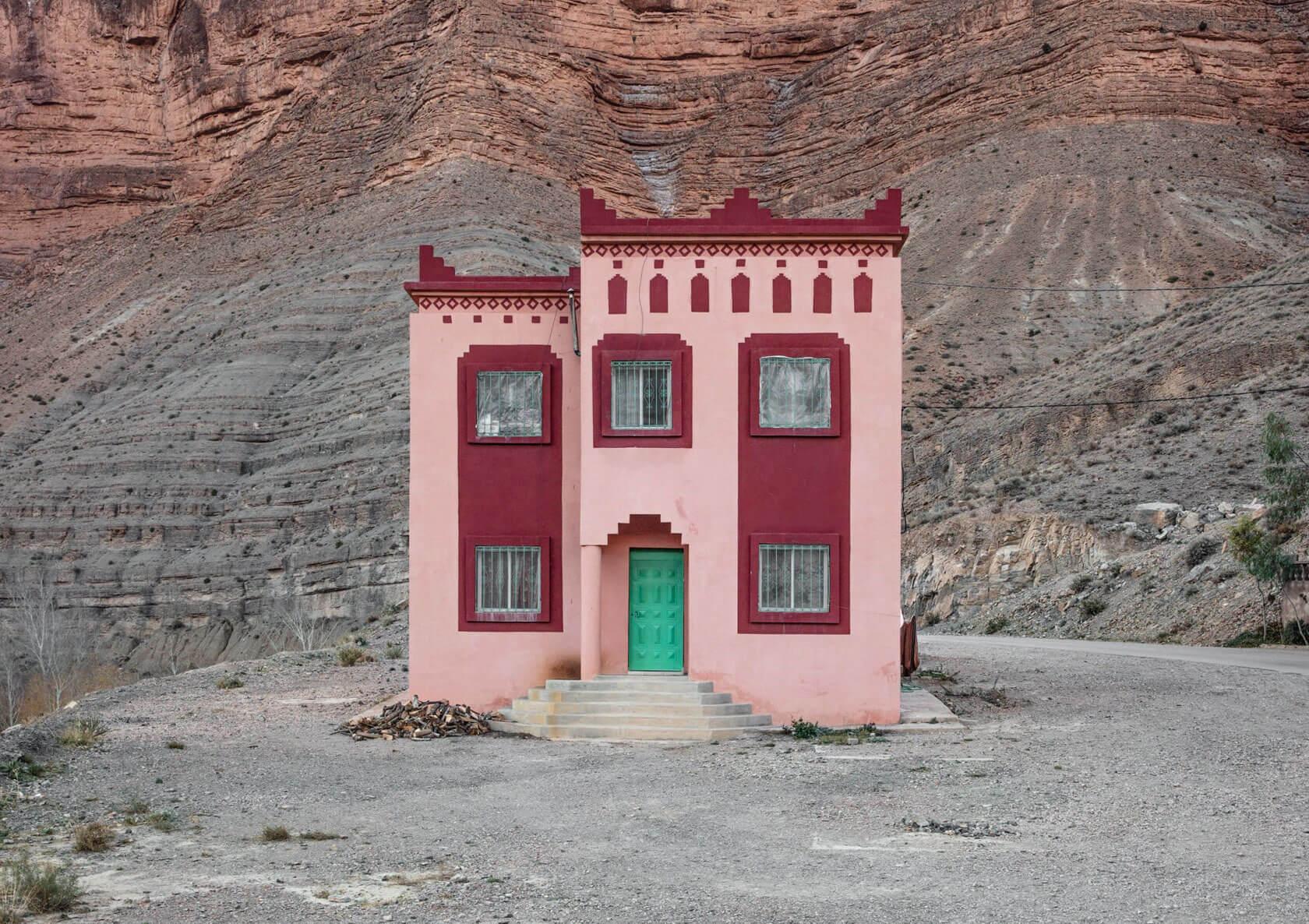 Pink and burgundy house with a bright green door standing against a dramatic layered rocky mountainside.