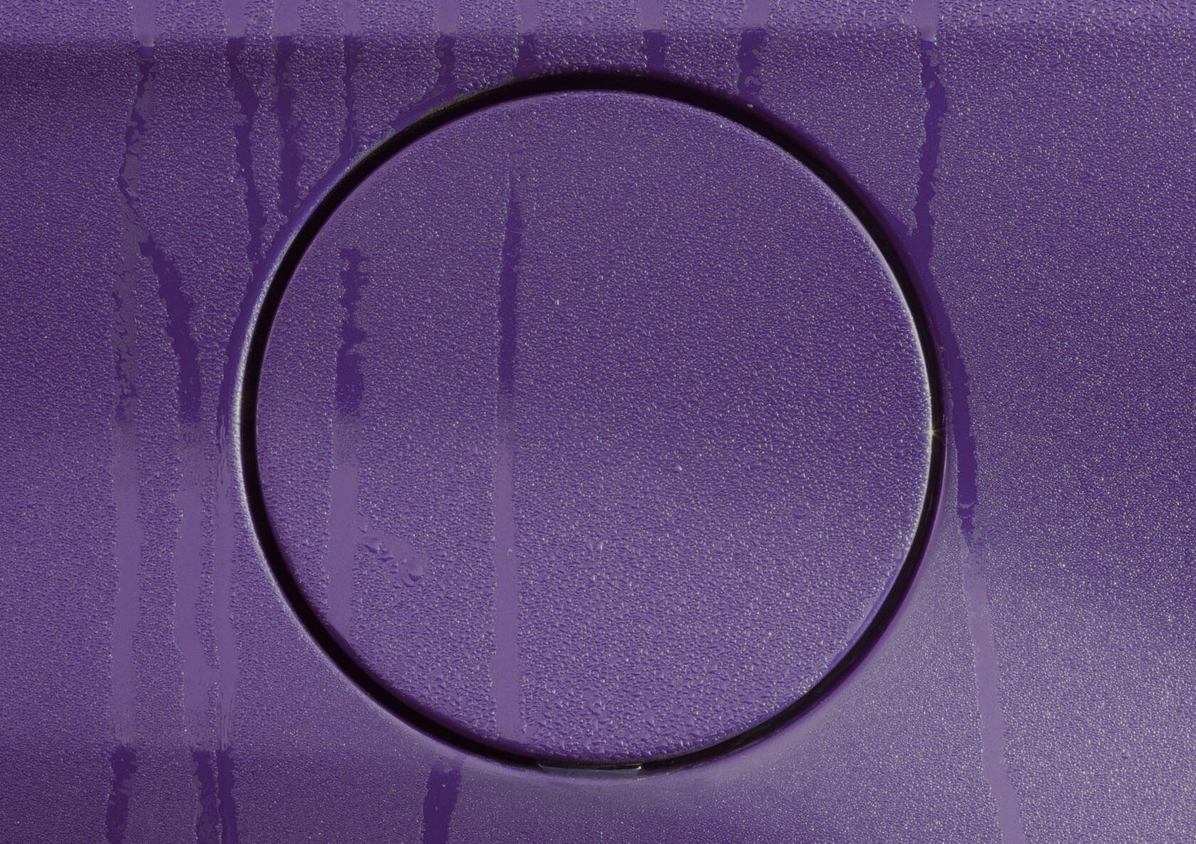 Close-up of a circular fuel cap outlined against a purple car surface covered in condensation and water streaks.