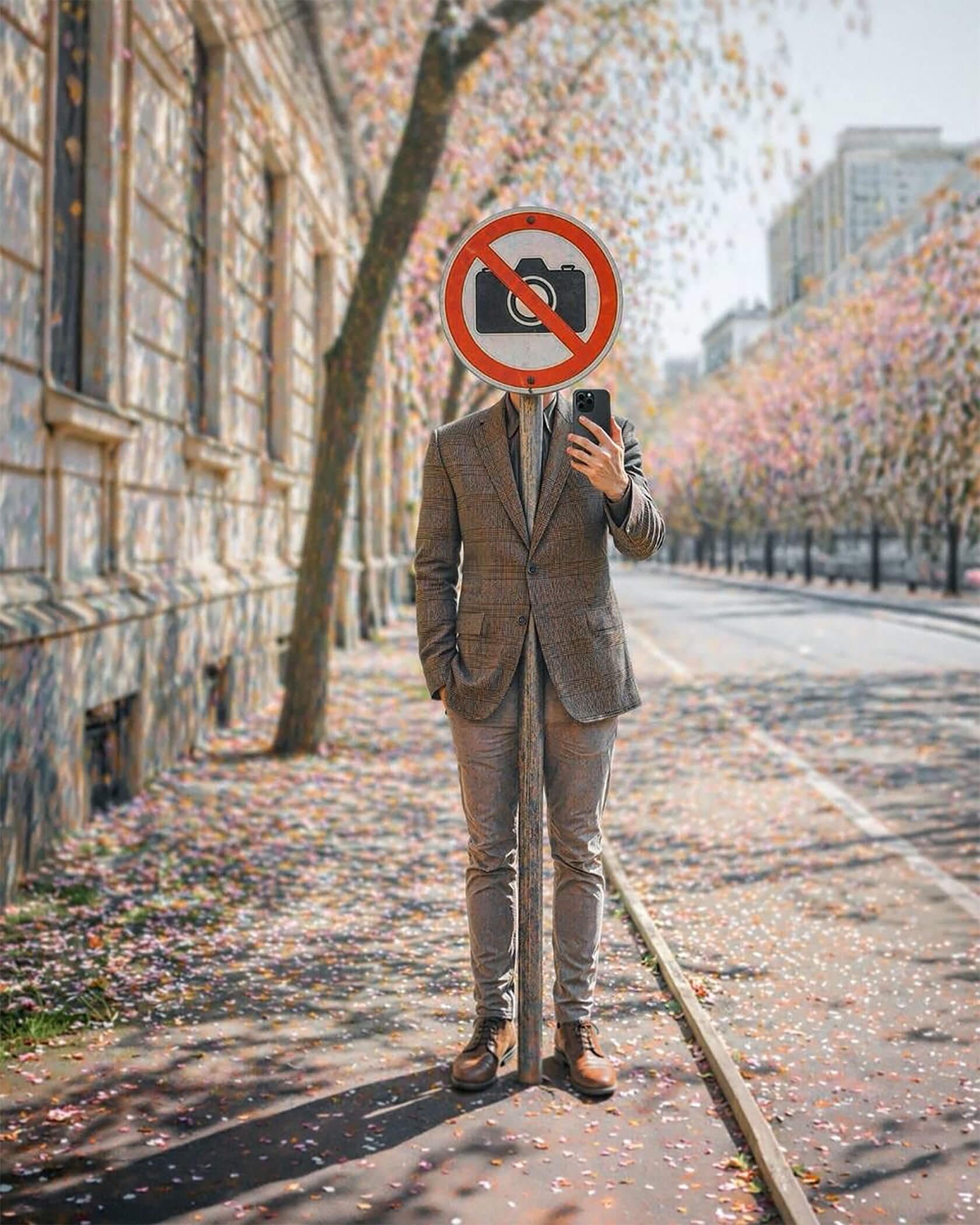 A surreal street portrait of a suited person taking a selfie, their head replaced by a red and white “no photography” sign.