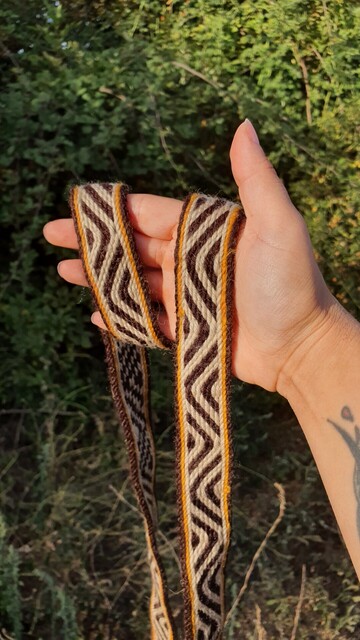 A hand woven trim made on a rigid heddle loom and tablet weaving technique, using merino wool in brown, white and yellow.