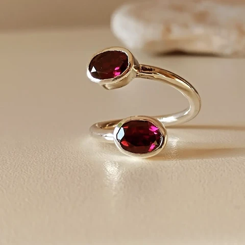 A silver open ring, on it's edges it has two dark red stones.