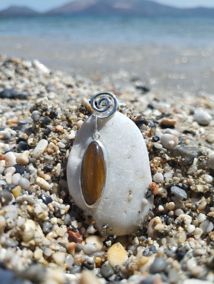 an earring on a pebble. It's a brown oval gemstone hanging from a silver spiral. 